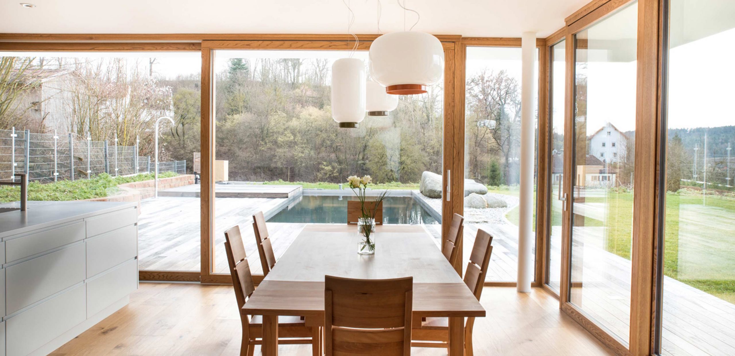 Blick auf den Essbereich des Einfamilienhauses WEL mit Über-Eck-Verglasung und Hebeschiebetüren. Der komplett verglaste Essbereich geniesst den Blick auf Terrasse und Garten inklusive Pool.